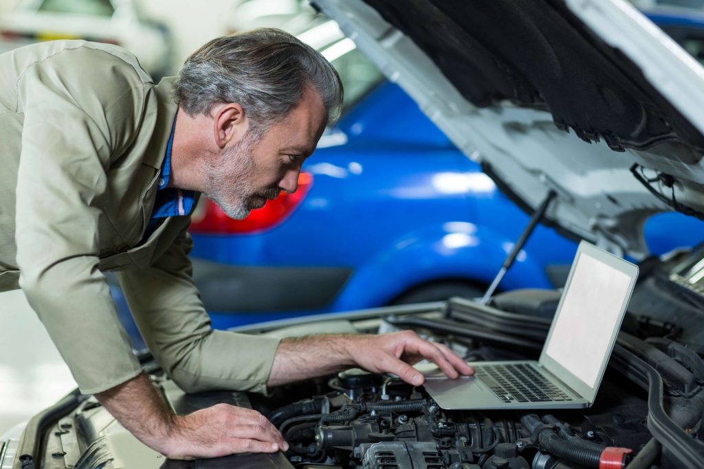 mechanic using laptop while servicing car engine min 1